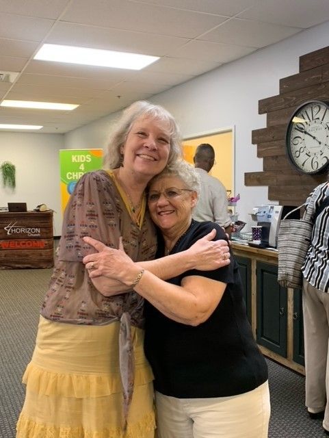 Two women hugging in a room with a clock on the wall