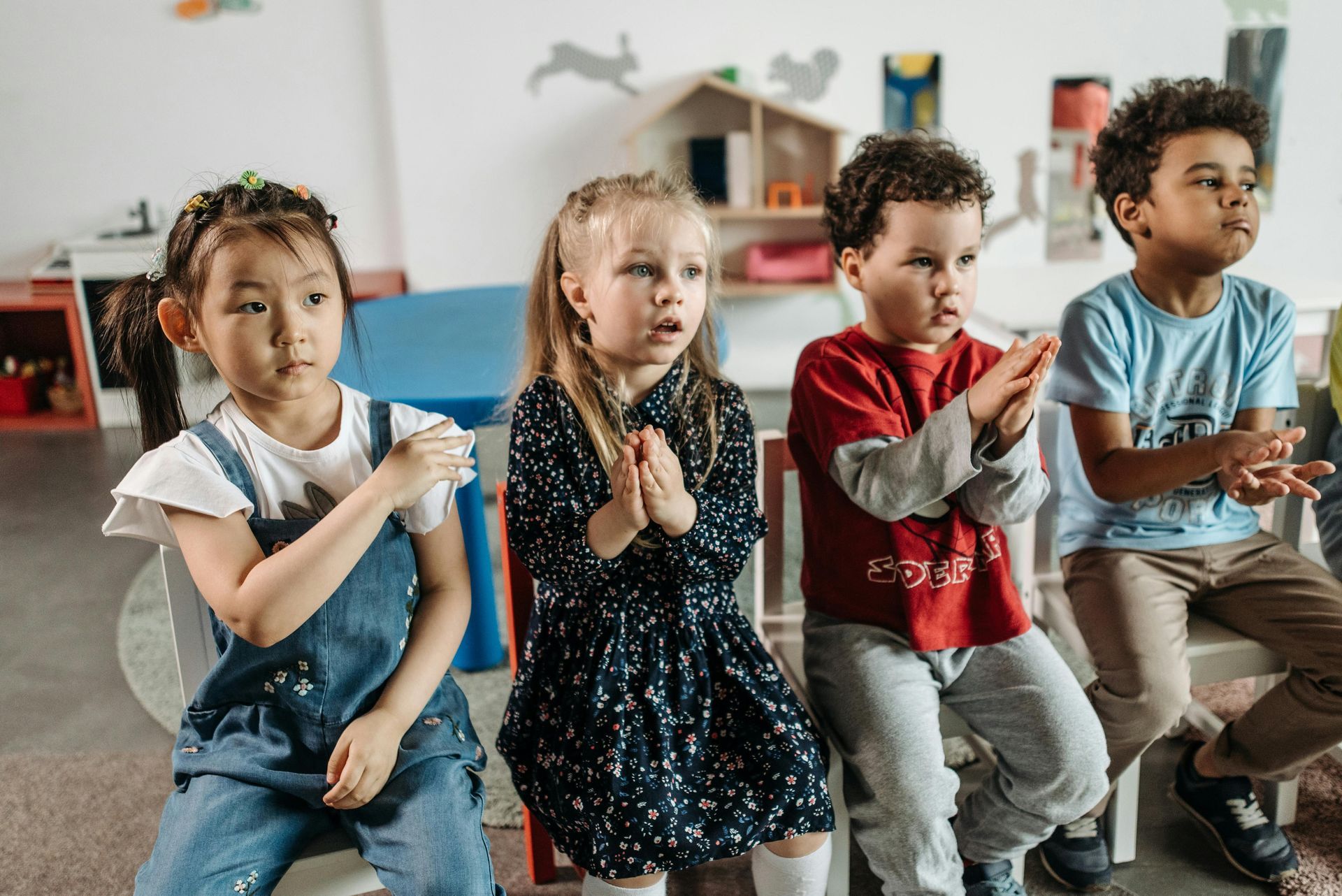 Jonge kinderen die naast elkaar op een bankje zitten in een klaslokaal en klappen.