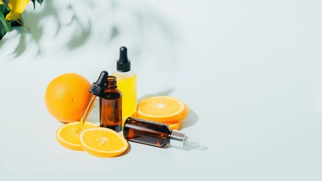 A bottle of vitamin c serum surrounded by oranges and lemons on a table.