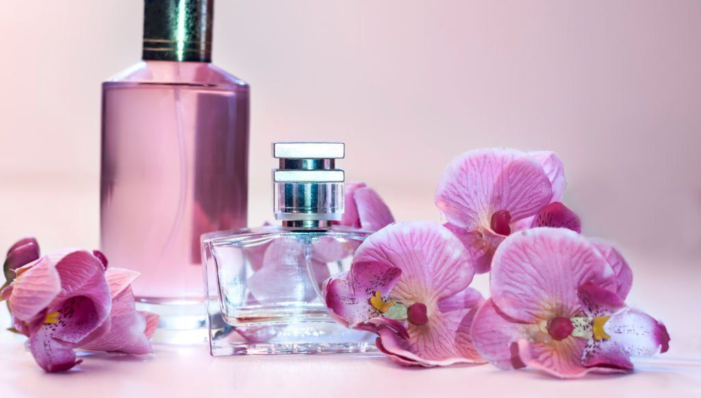 Two bottles of perfume and pink flowers on a table.