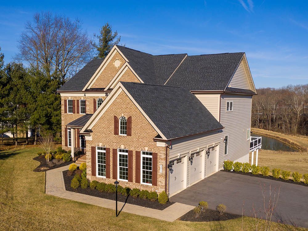 An aerial view of a large brick house with a garage and a pond in the background.