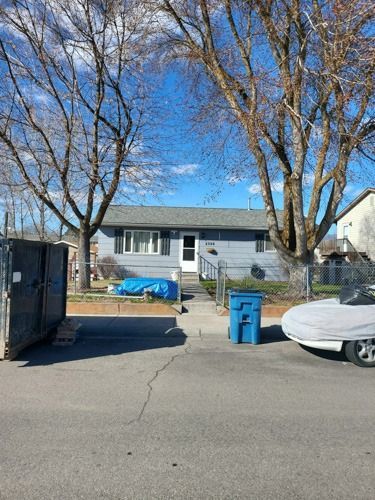 A blue trash can is parked in front of a house.