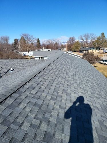 A man is taking a picture of his shadow on the roof of a house.