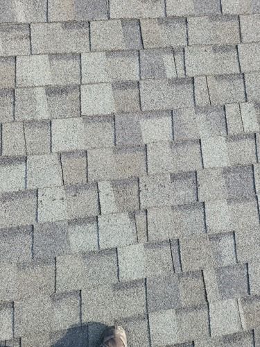 A person is standing on a roof with shingles that are missing.