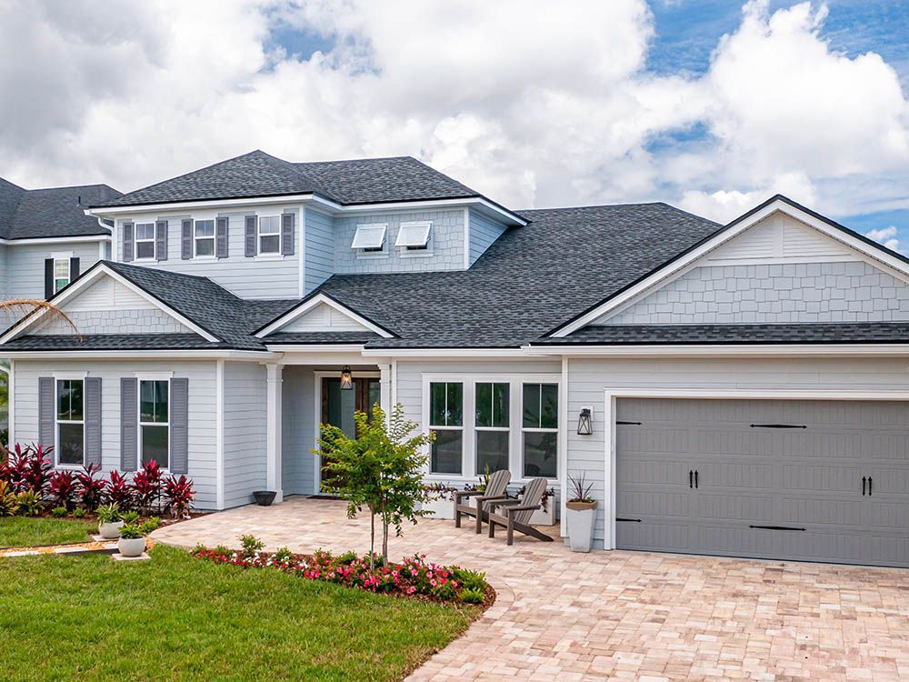 A large white house with a gray garage door and a brick driveway.