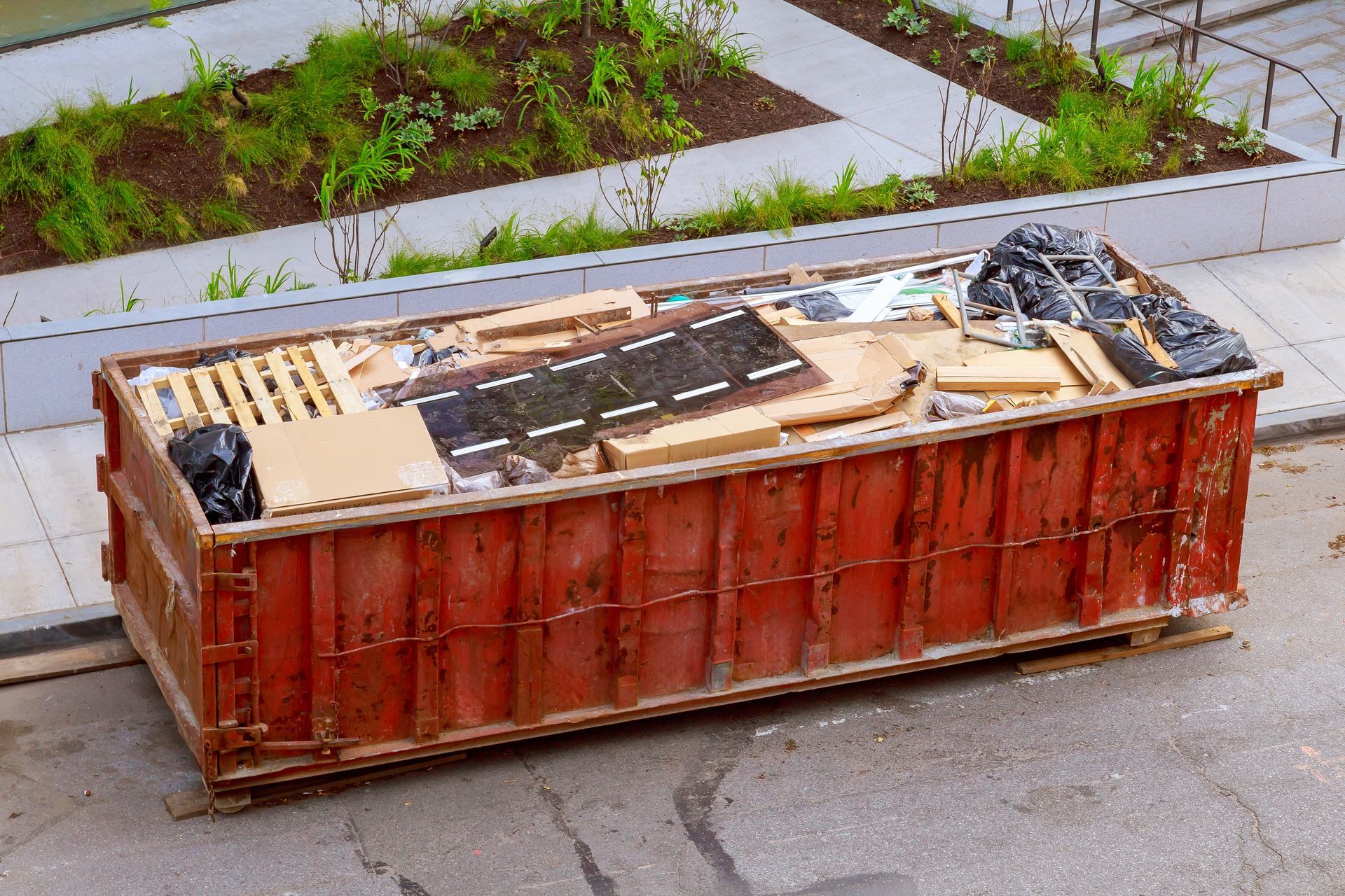 Red dumpster filled with construction debris, parked on asphalt.