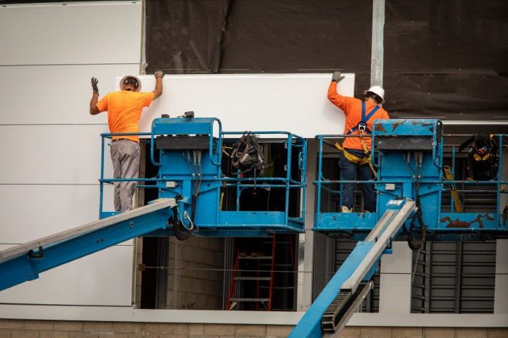 An image of two workers in boom lifts installing drywall