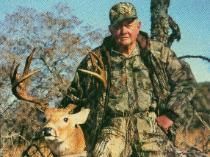 A man in a camo jacket is holding a deer.