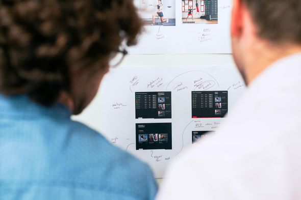 Two men are looking at a whiteboard with pictures on it.