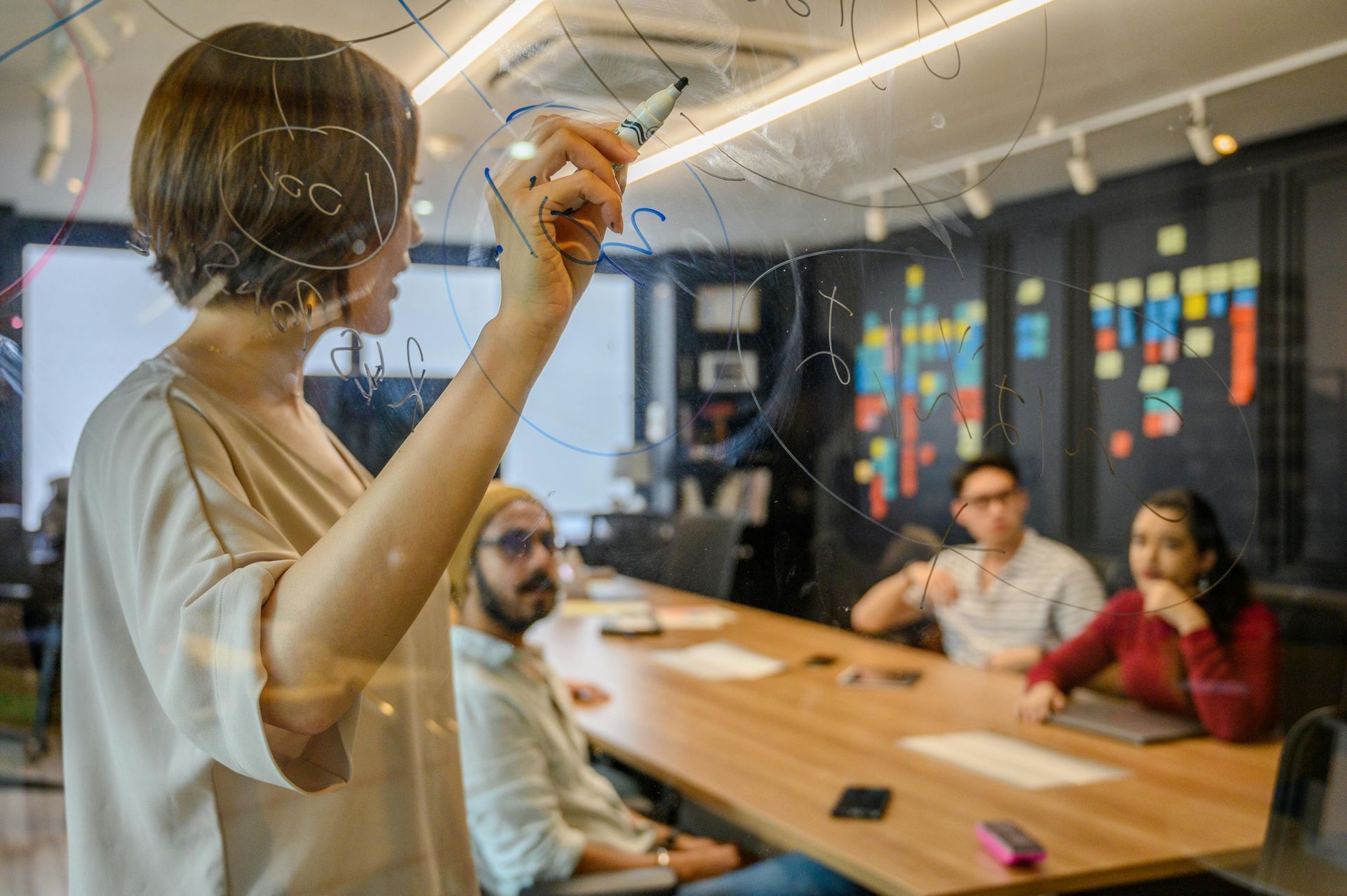 A woman is writing on a glass board in front of a group of people.