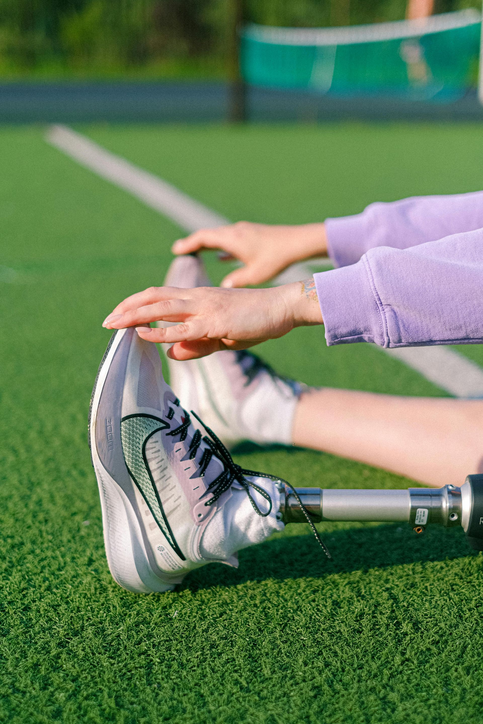 A person with a prosthetic leg is stretching their legs on a tennis court.