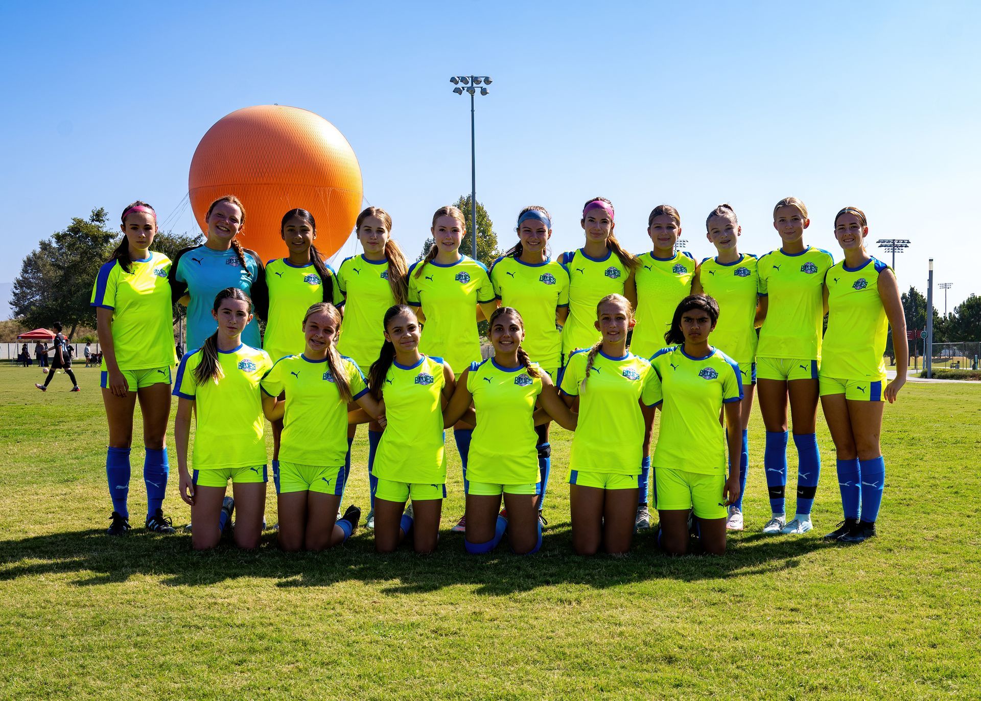 A group of female SC Blues soccer players posing for a picture with an orange balloon in the background