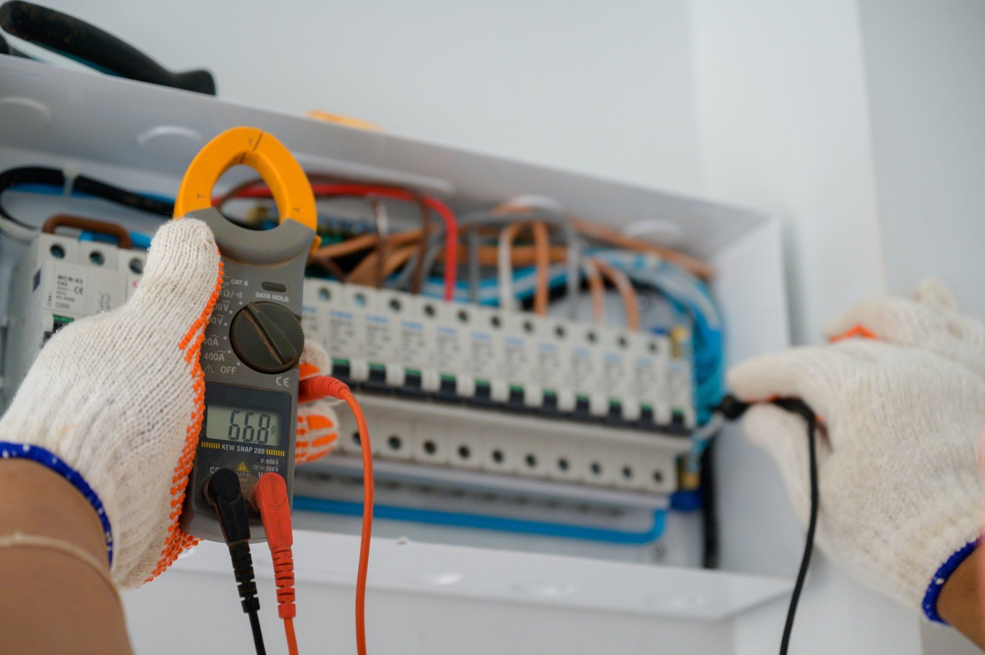 A person is holding a clamp meter in front of an electrical box.