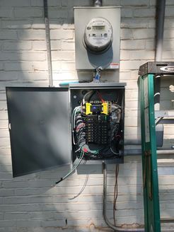 A electrical box is hanging on a brick wall next to a ladder.