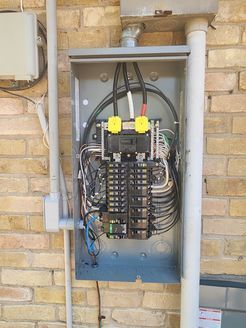 An electrical box is hanging on a brick wall.