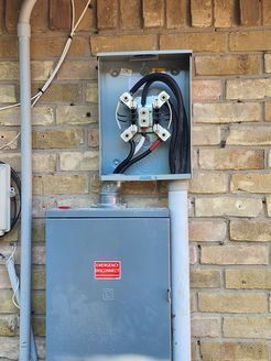 An electrical box is attached to a brick wall.