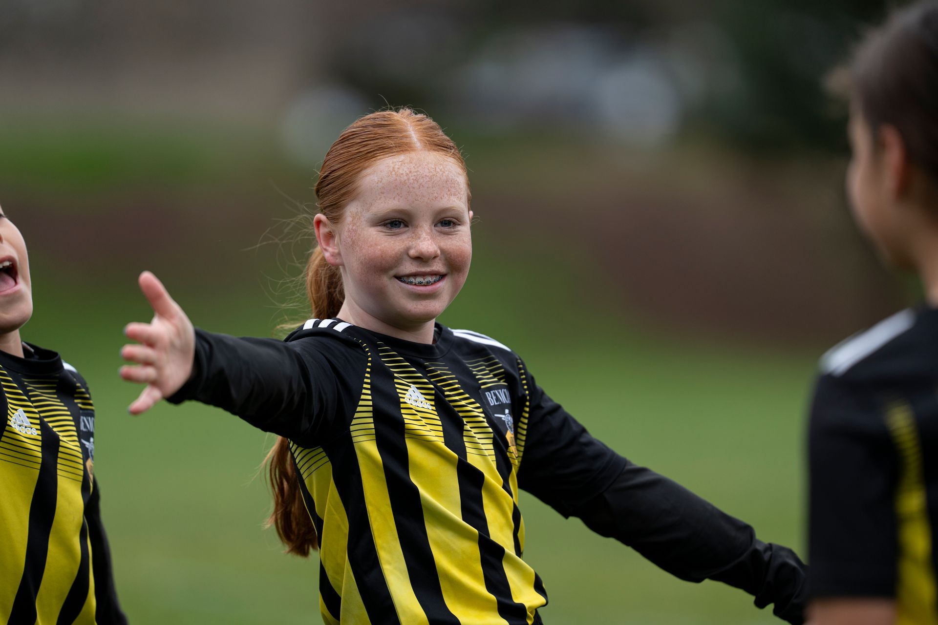 Girl in yellow and black soccer uniform, smiling, giving a thumbs up on a field.