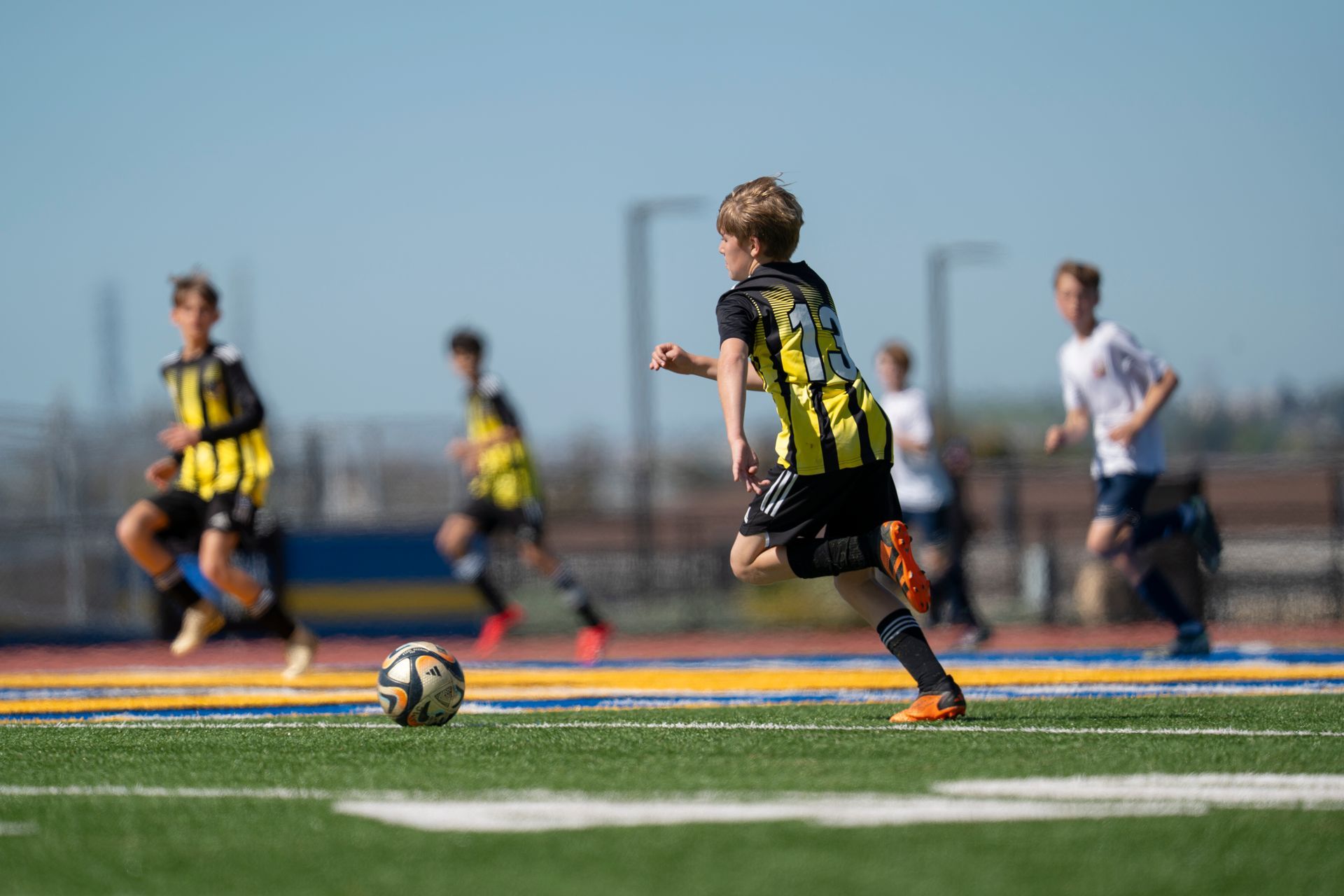 Soccer player in black and yellow jersey dribbles the ball on green field, followed by teammates and opponents.
