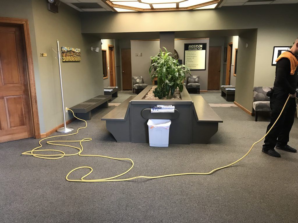 A man is cleaning a waiting room with a yellow hose.