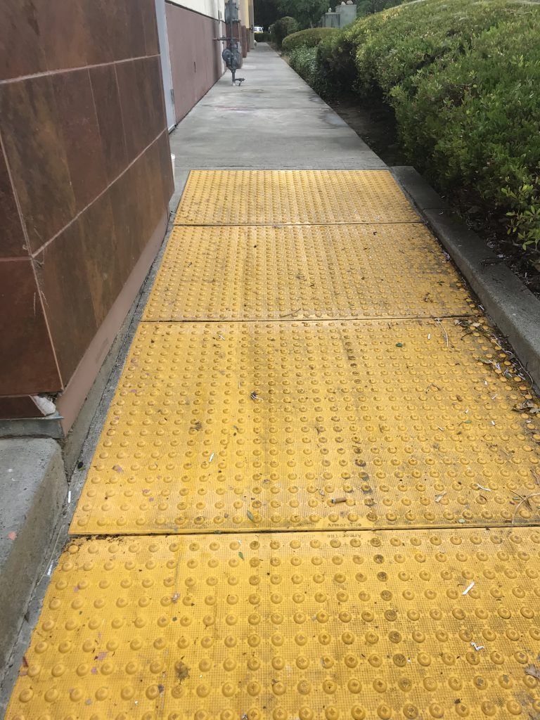 A sidewalk with a yellow curb and a person walking down it.