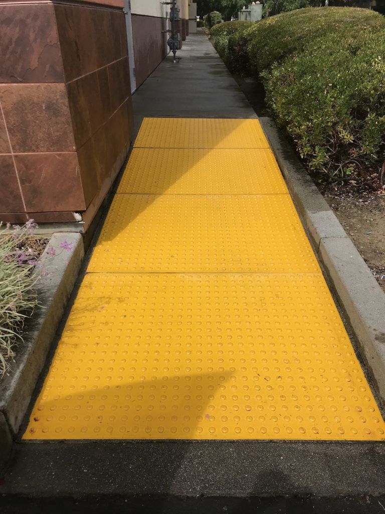 A yellow walkway is painted on the sidewalk next to a building.