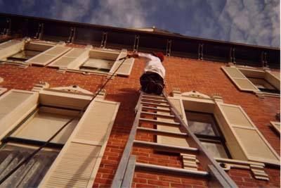 A man on a ladder painting a brick building