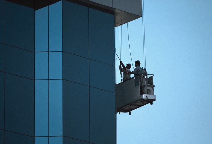 Two men are cleaning the windows of a tall building.