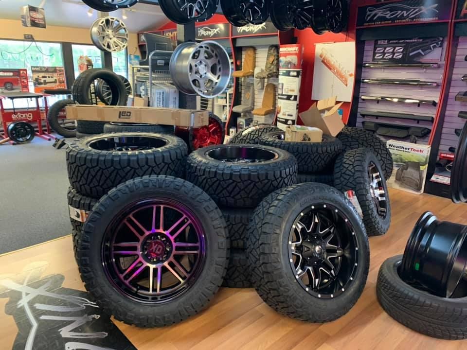 Tires and black rims stacked in a store, purple and black rims are prominent in the foreground.