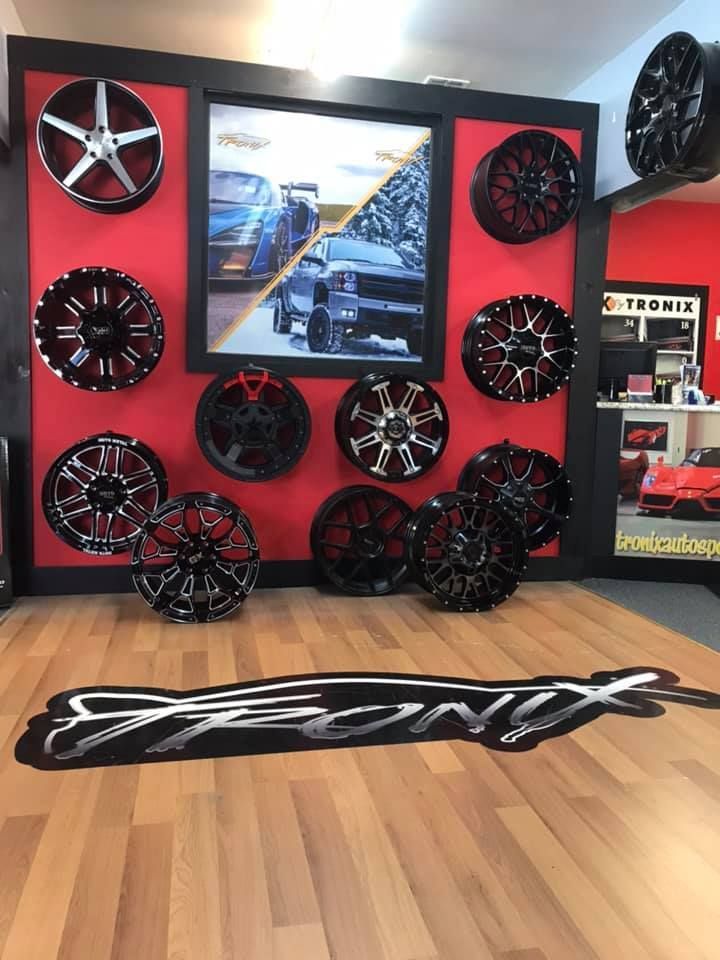 Car wheel display on red wall, black and silver wheels, rug on wooden floor, shop setting.