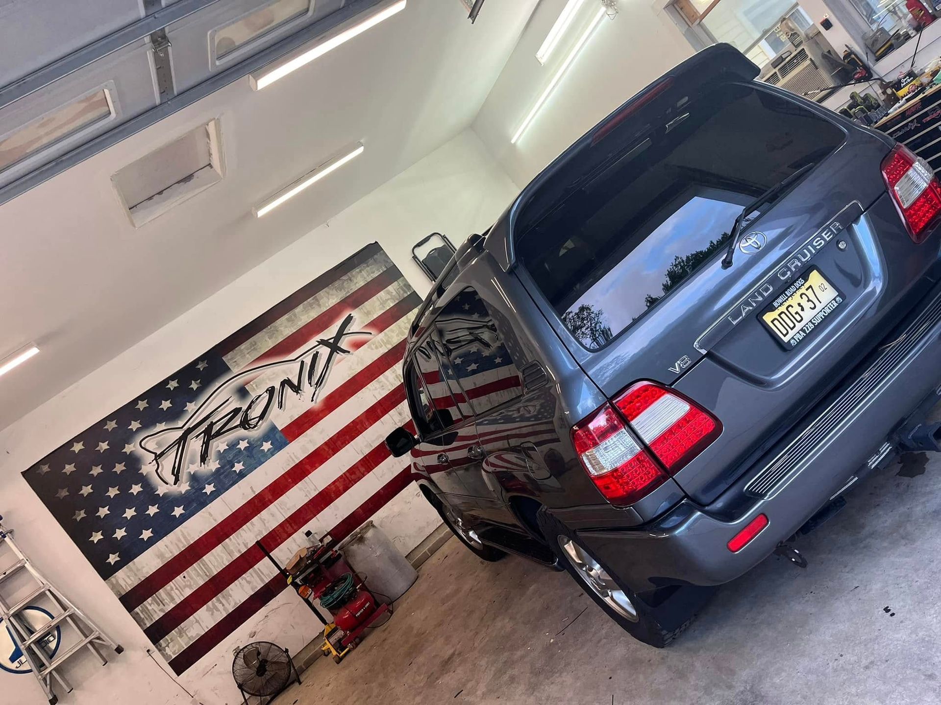 Dark grey SUV parked inside a garage, with an American flag and logo on the wall.