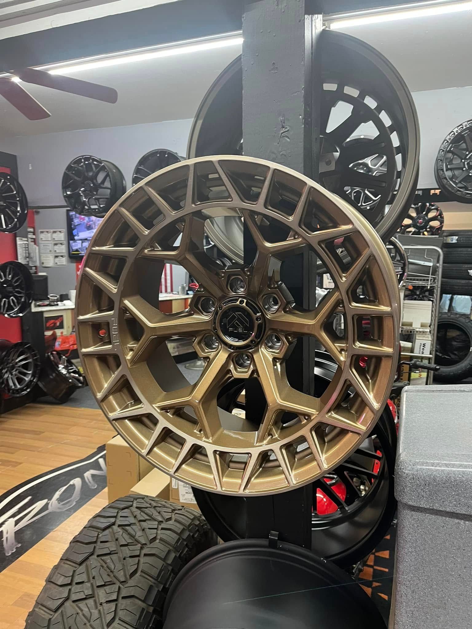 Bronze-colored alloy wheel displayed indoors, other wheels in background.