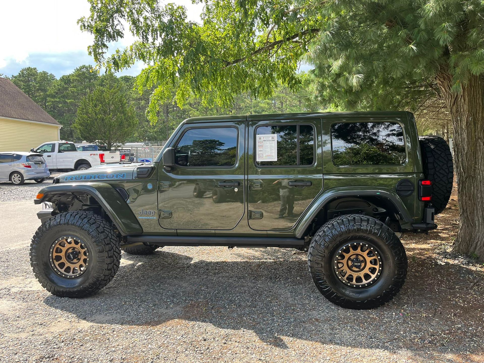 Green Jeep Wrangler with bronze wheels, parked on gravel.
