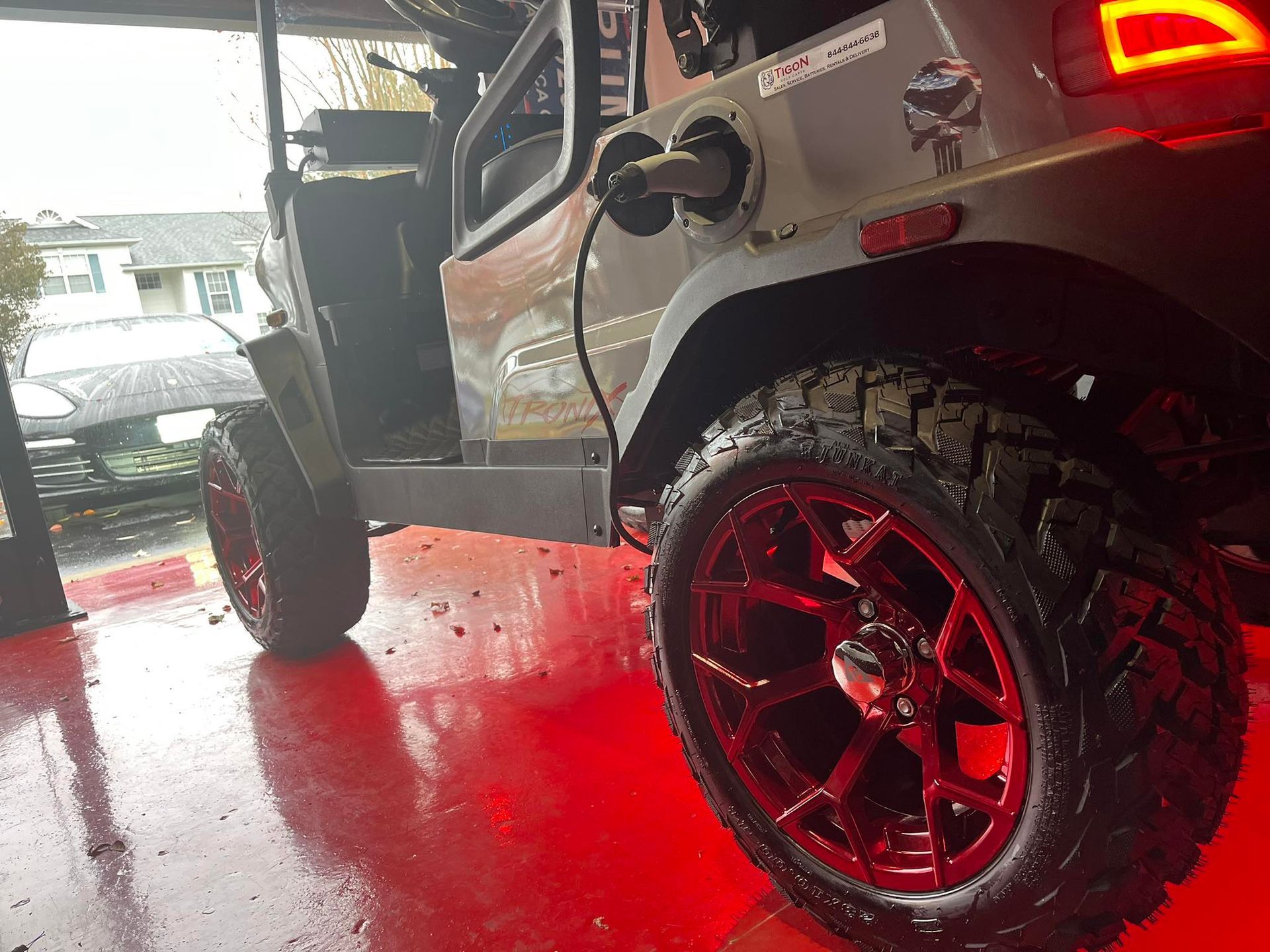 Gray Jeep with red rims parked on a red floor. Gas tank door open.