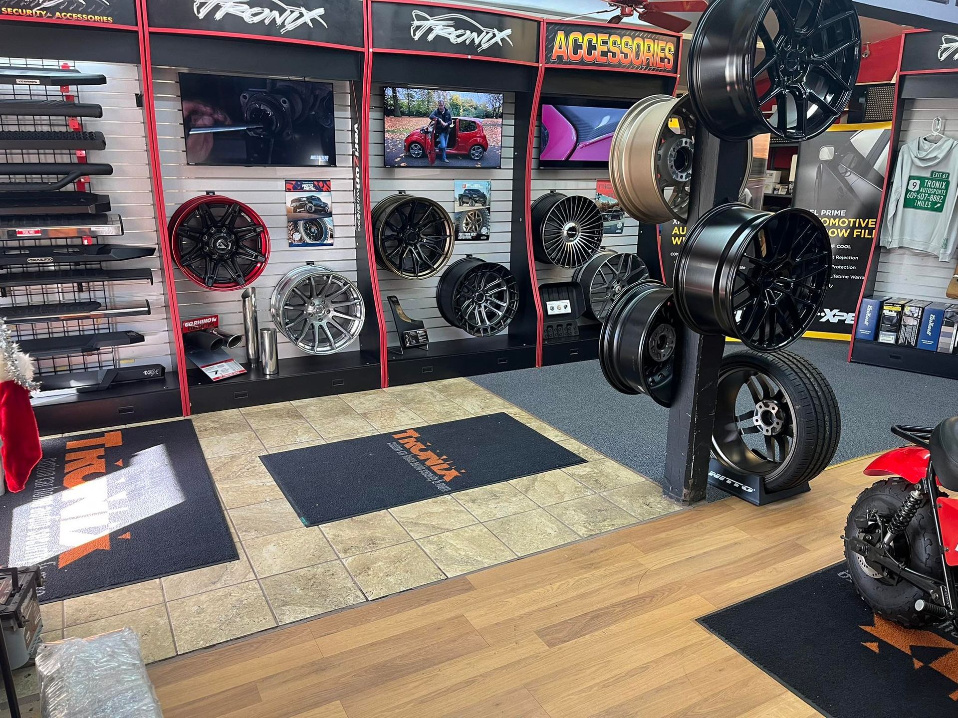 Interior of a car accessories store: wheels on display, shelves with products, a motorcycle, and various accessories.
