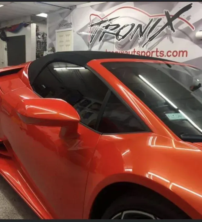 Orange convertible car in a garage with tinted windows. Black top.