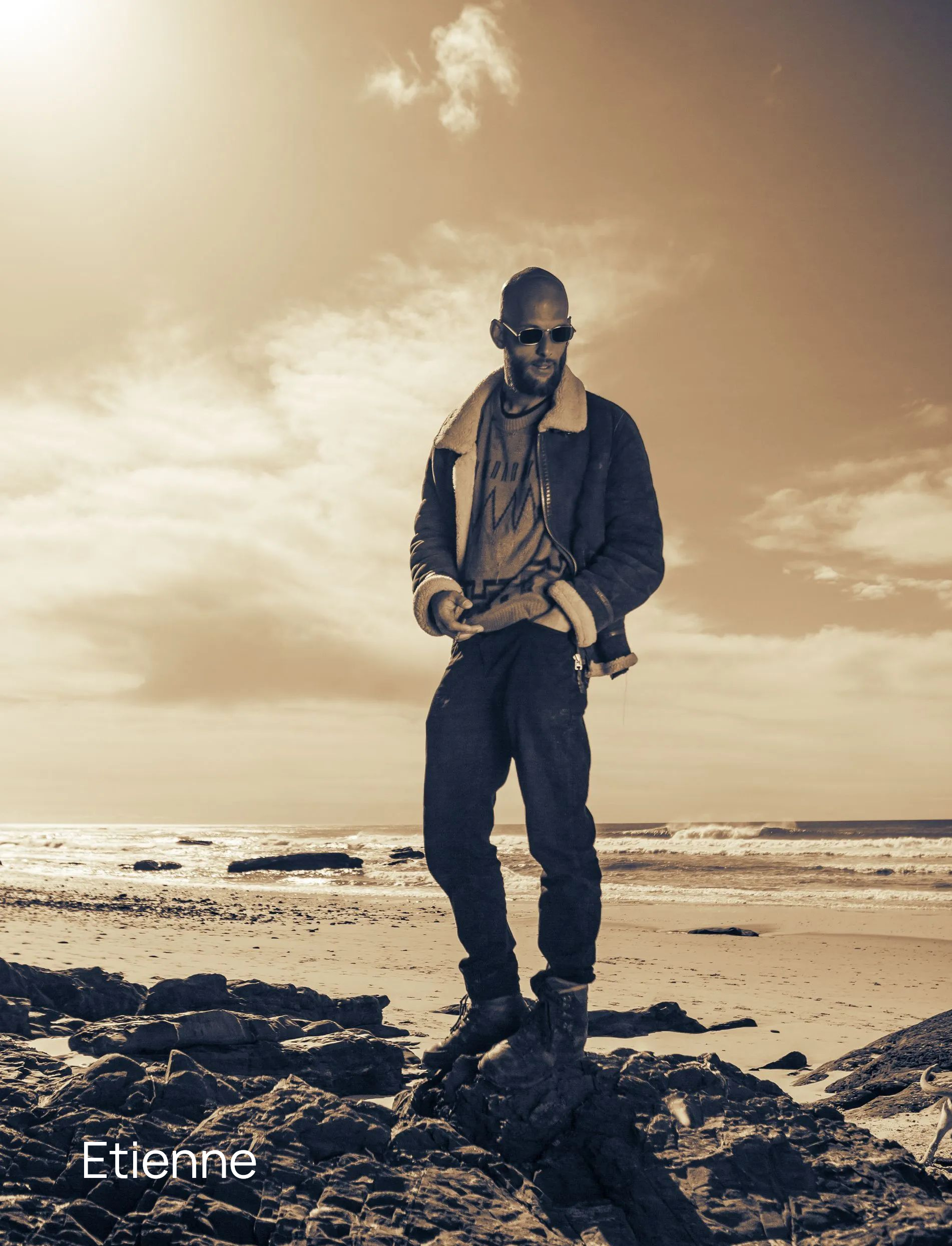 sepia Fotografie eines coolen Mannes mit Glatze und Sonnenbrille, der auf einem Stein steht am Strand an der Algarve in Portugal