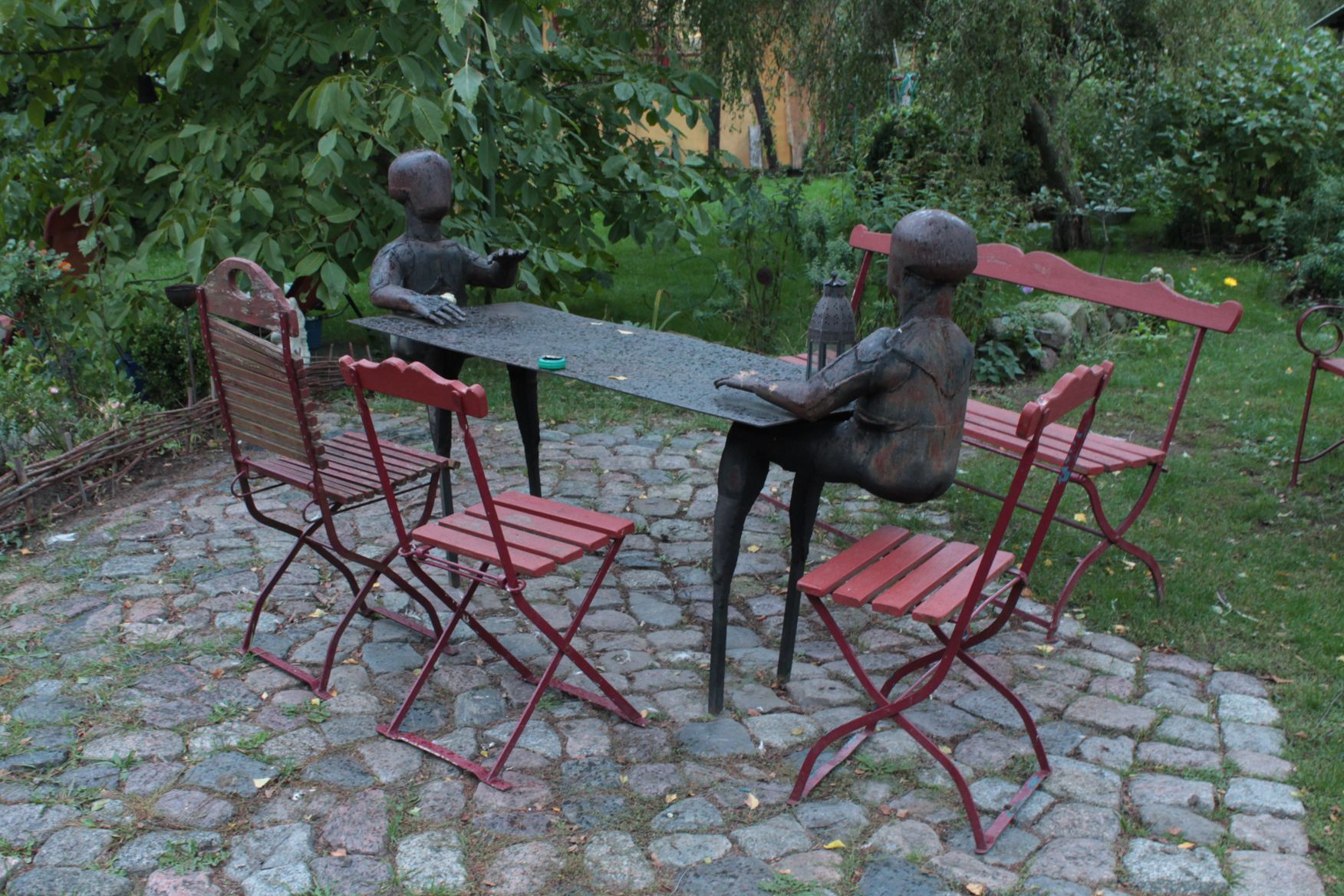 Eine Statue von zwei Kindern, die an einem Tisch mit roten Stühlen sitzen