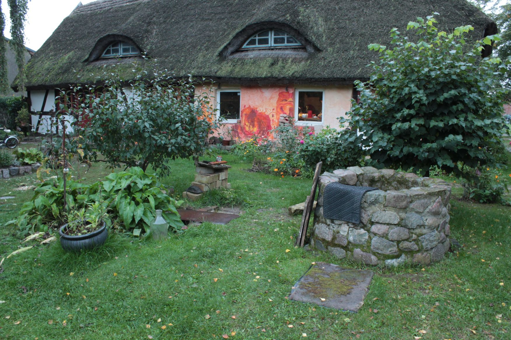 Ein strohgedecktes Haus mit einem Brunnen davor