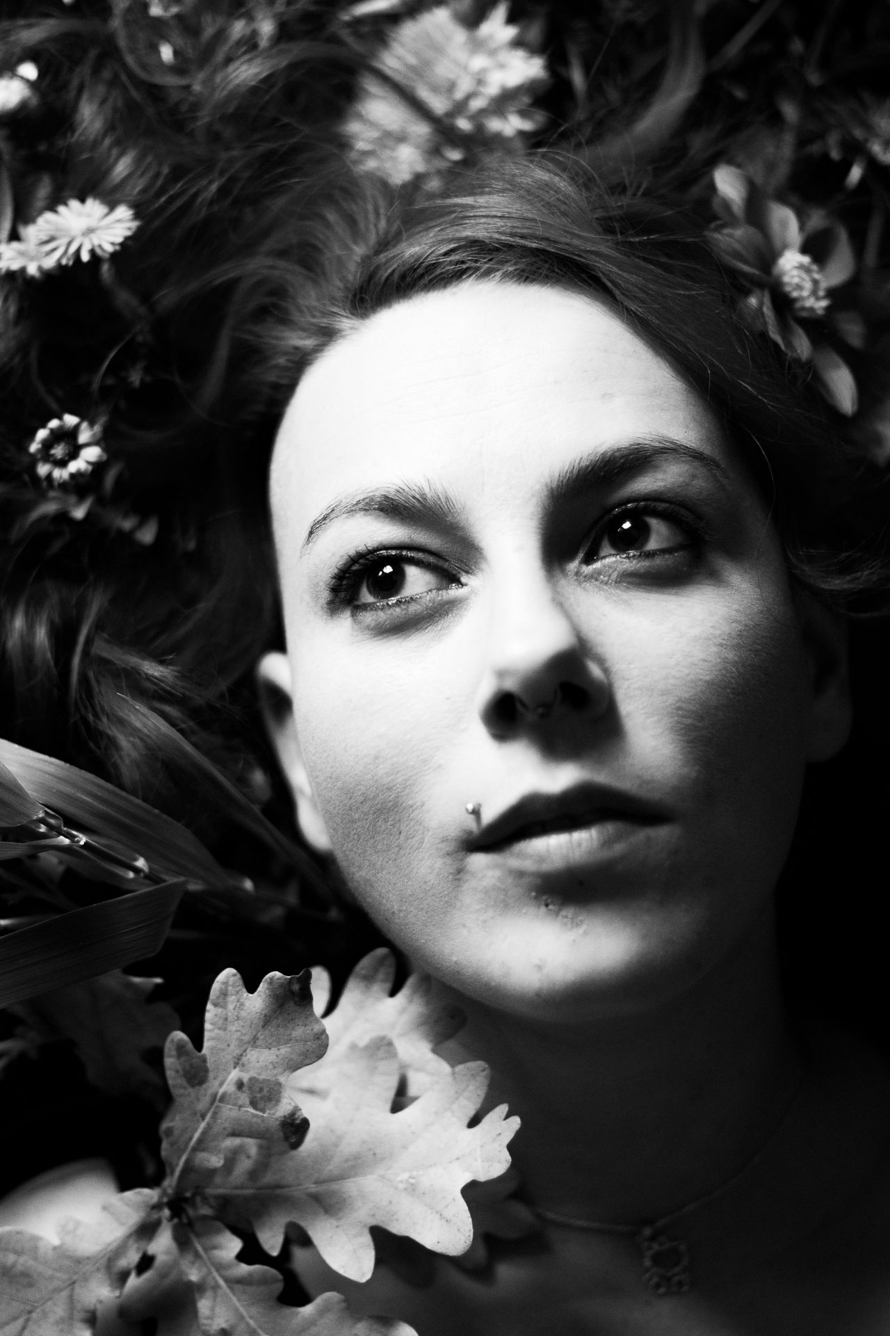 Konzeptionelle Fotografie Schwarzweißfoto einer Frau, die im Gras mit Blumen liegt