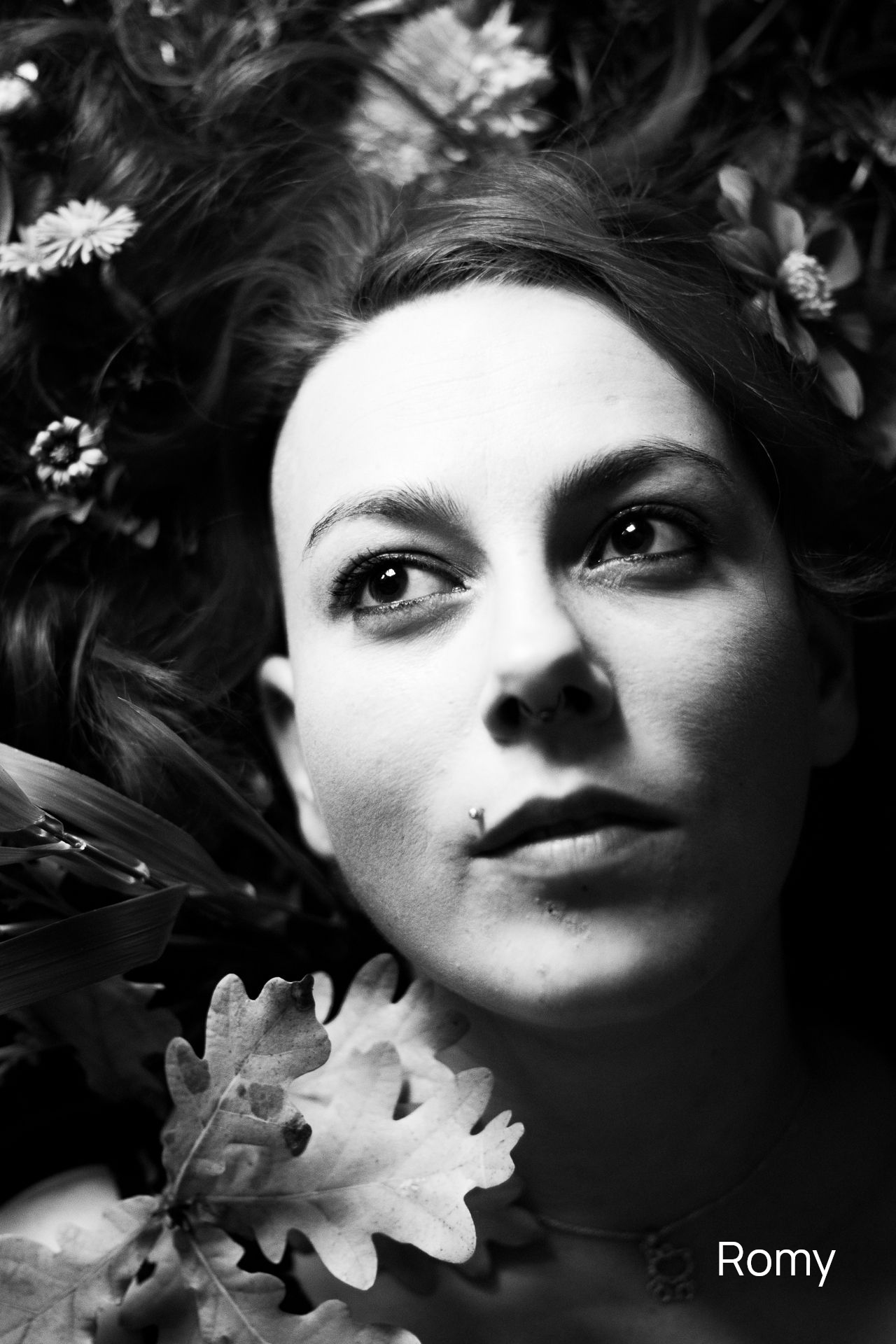 Konzeptionelle Fotografie Schwarzweißfoto einer Frau, die im Gras mit Blumen liegt