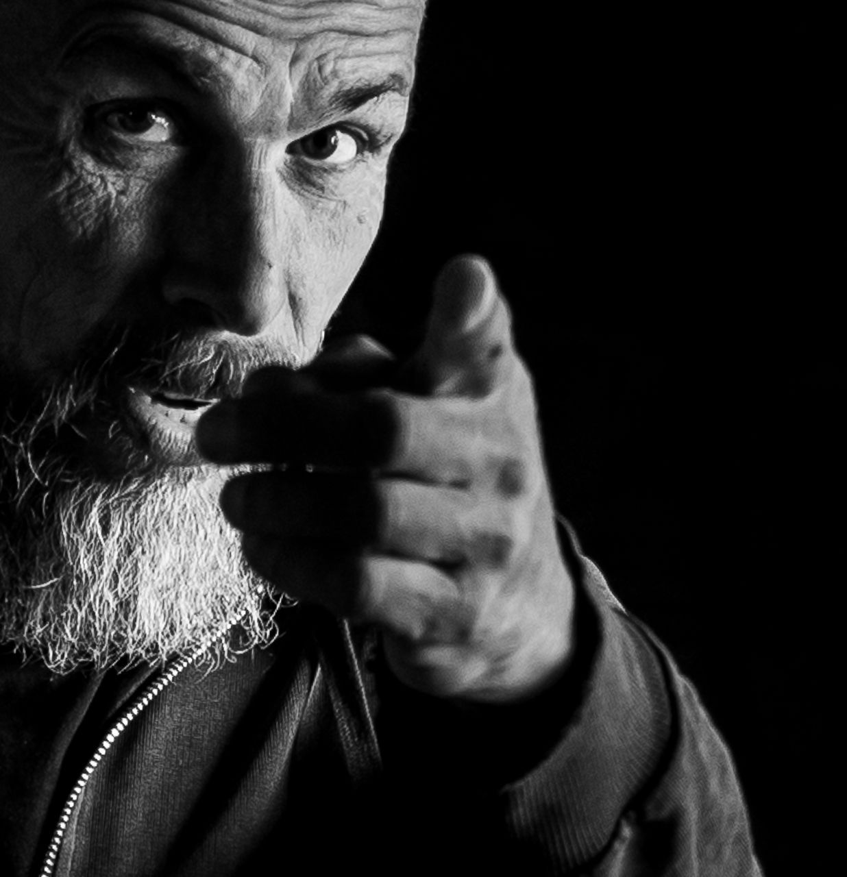 Schwarzweißfoto Porträt eines Mannes mit Bart der mit dem Finger in die Kamera zeigt