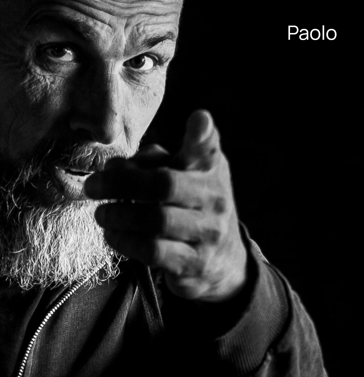 Schwarzweißfoto Porträt eines Mannes mit Bart der mit dem Finger in die Kamera zeigt