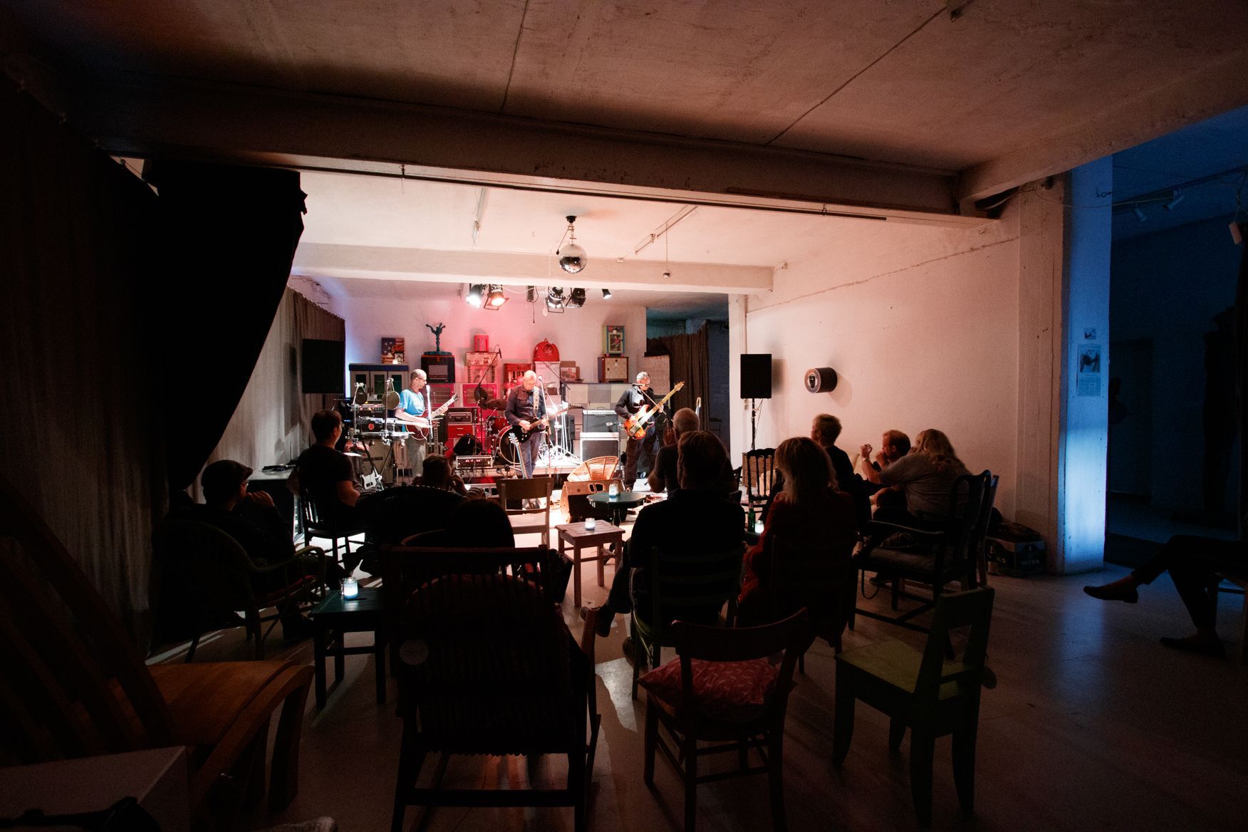 Eine Gruppe von Menschen sitzt in einem dunklen Raum und hört einer Band zu.