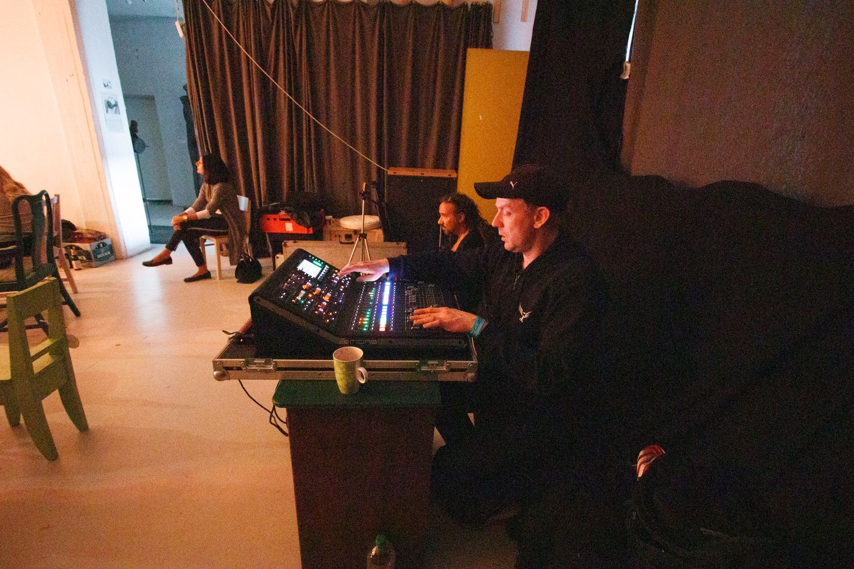 Ein Mann mit schwarzem Hut sitzt an einem Schreibtisch in einem dunklen Raum