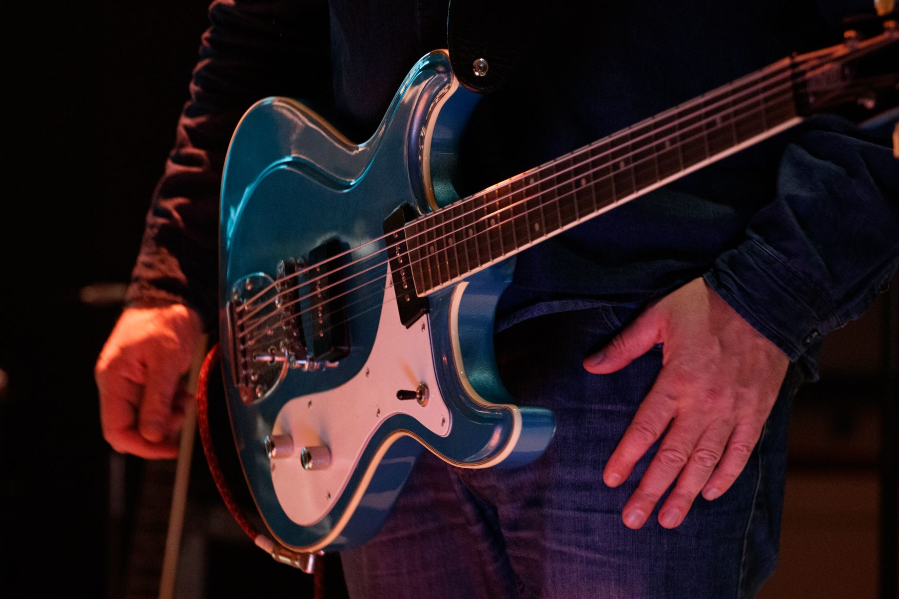 Ein Mann spielt in einem dunklen Raum eine blaue E-Gitarre