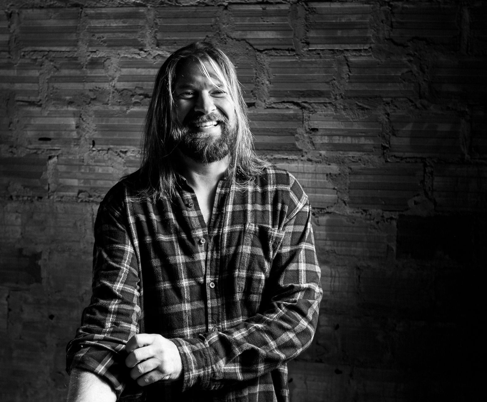 Schwarzweißfoto eines Mannes Surfers mit langen blonden Haaren, Bart, der die Ärmel seines karierten Hemdes hochkrempelt