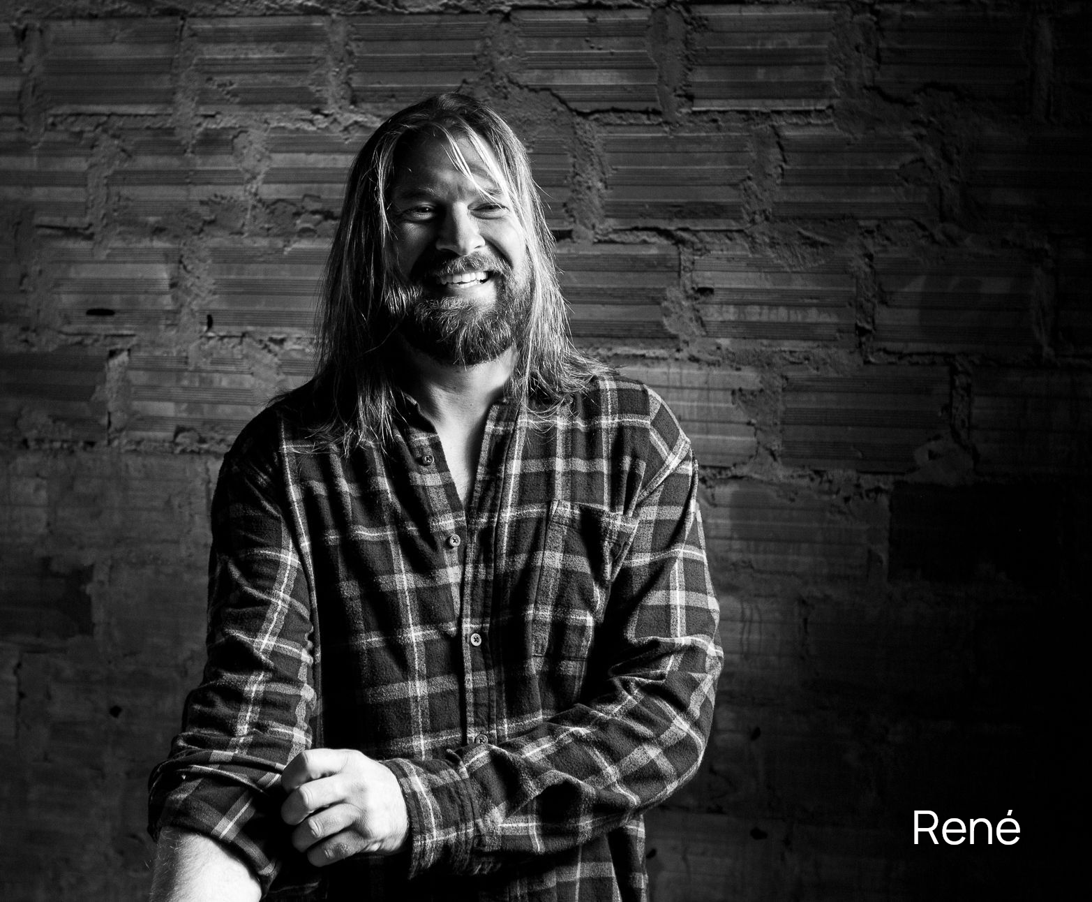 Schwarzweißfoto eines Mannes Surfers mit langen blonden Haaren, Bart, der die Ärmel seines karierten Hemdes hochkrempelt