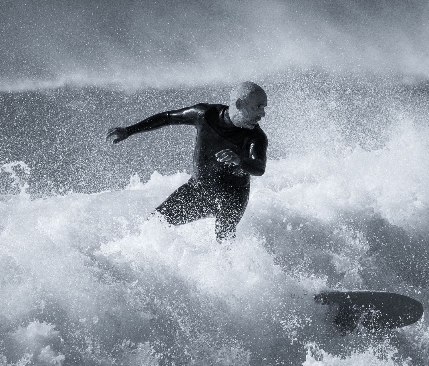 Ein portugiesischer Mann Local im Neoprenanzug reitet auf einem Surfbrett auf einer Welle in Barranco an der Algarve in Portugal
