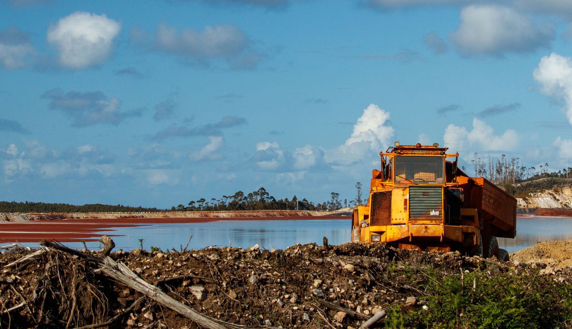 Ein großer gelber Lastwagen fährt eine unbefestigte Straße in der Nähe eines Gewässers entlang