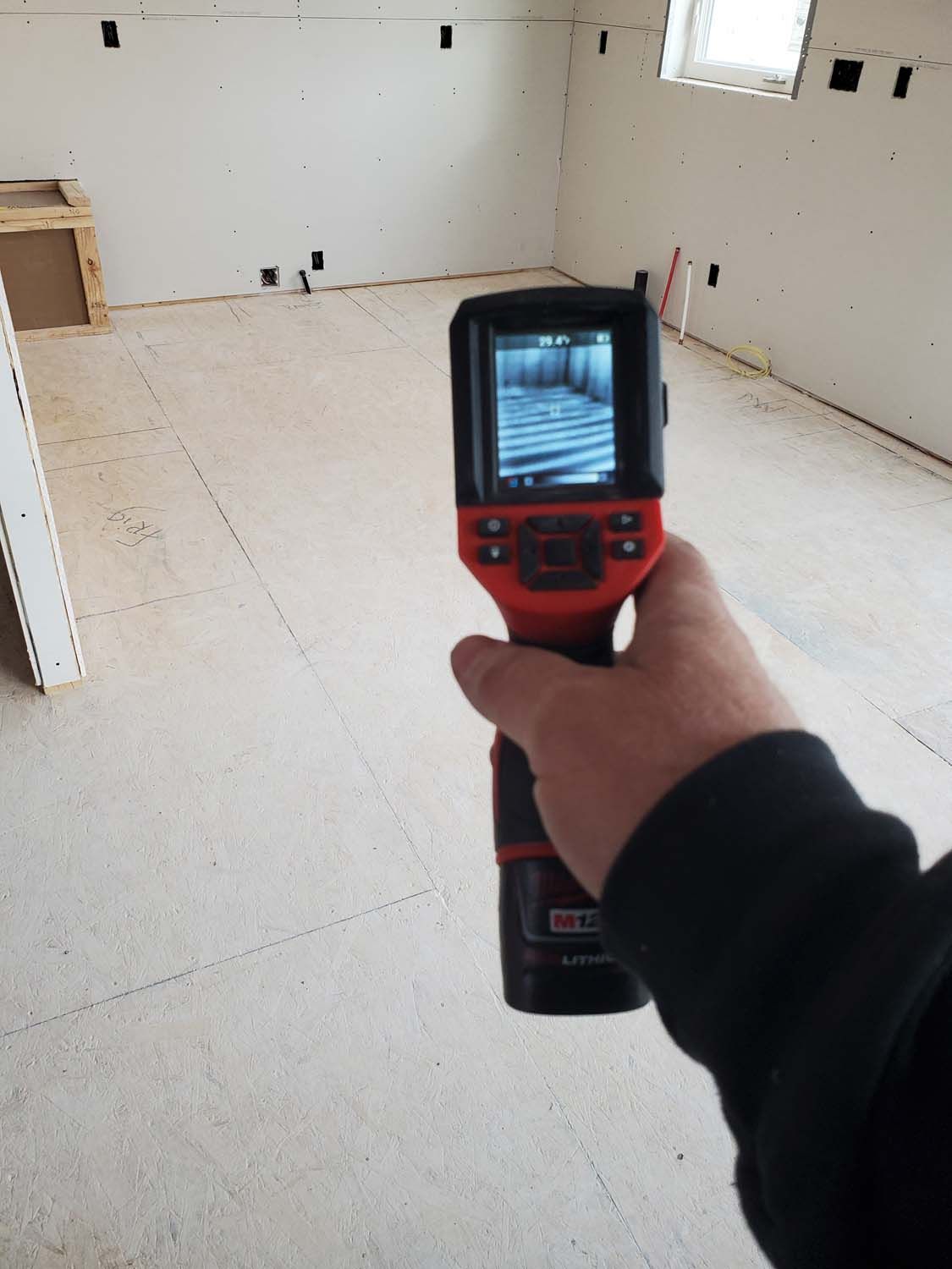 Person holding a thermal imaging camera in a room under construction, displaying the interior on its screen.